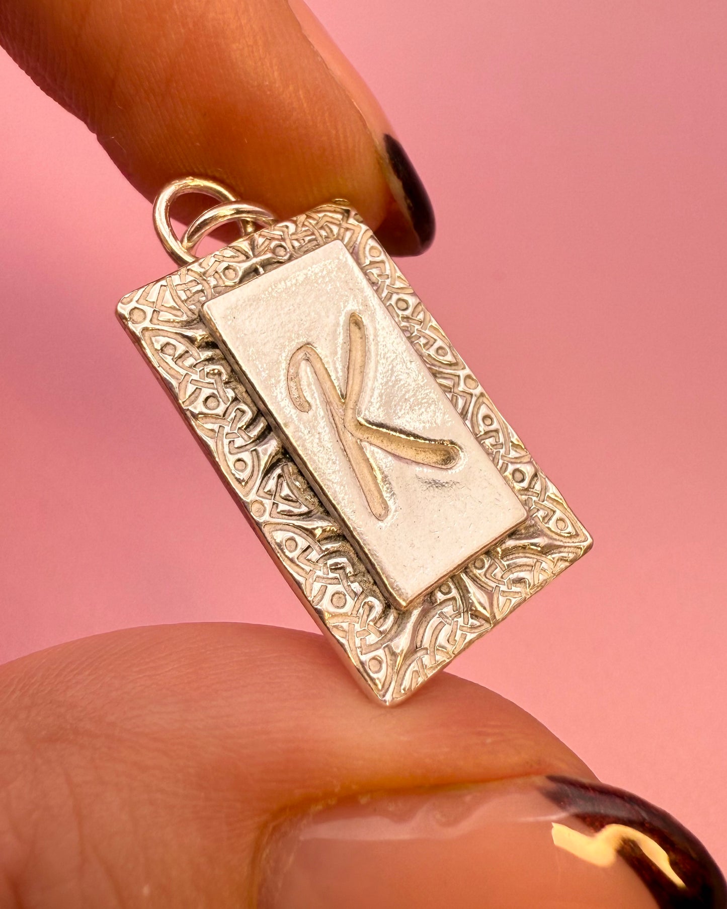 rectangular silver pendant with 'K' engraved on the front with celtic knot pattern on a pink background