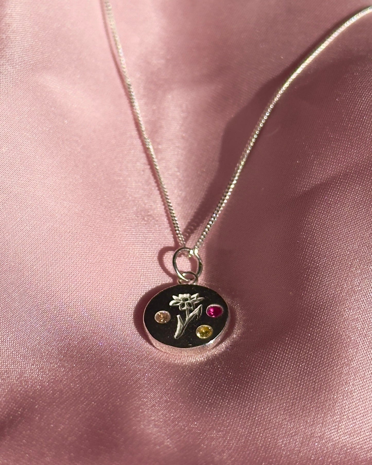 Necklace with a pendant featuring three colorful stones on a pink fabric background
