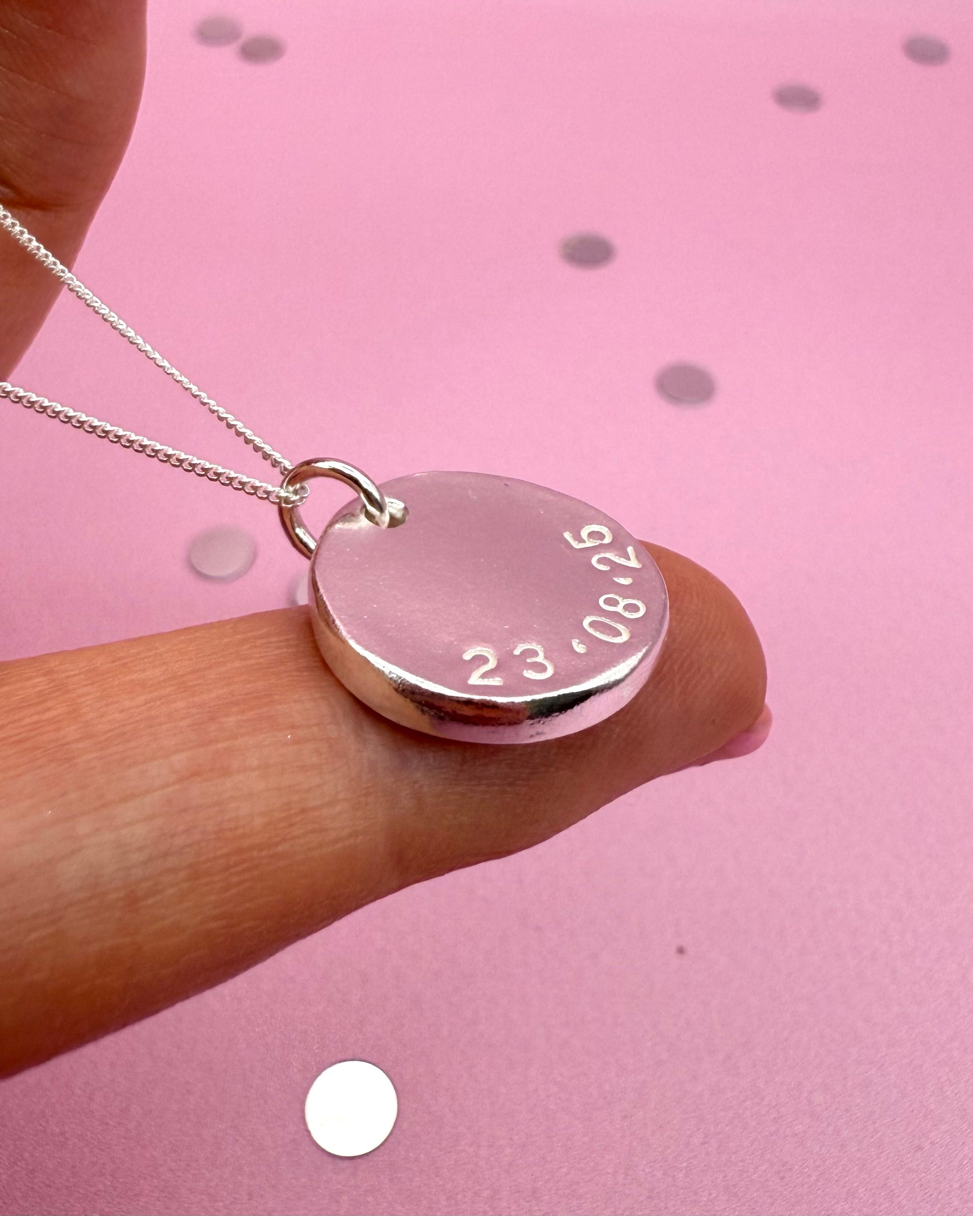 silver circular pendant stamped with a meaningful date in a circular shape