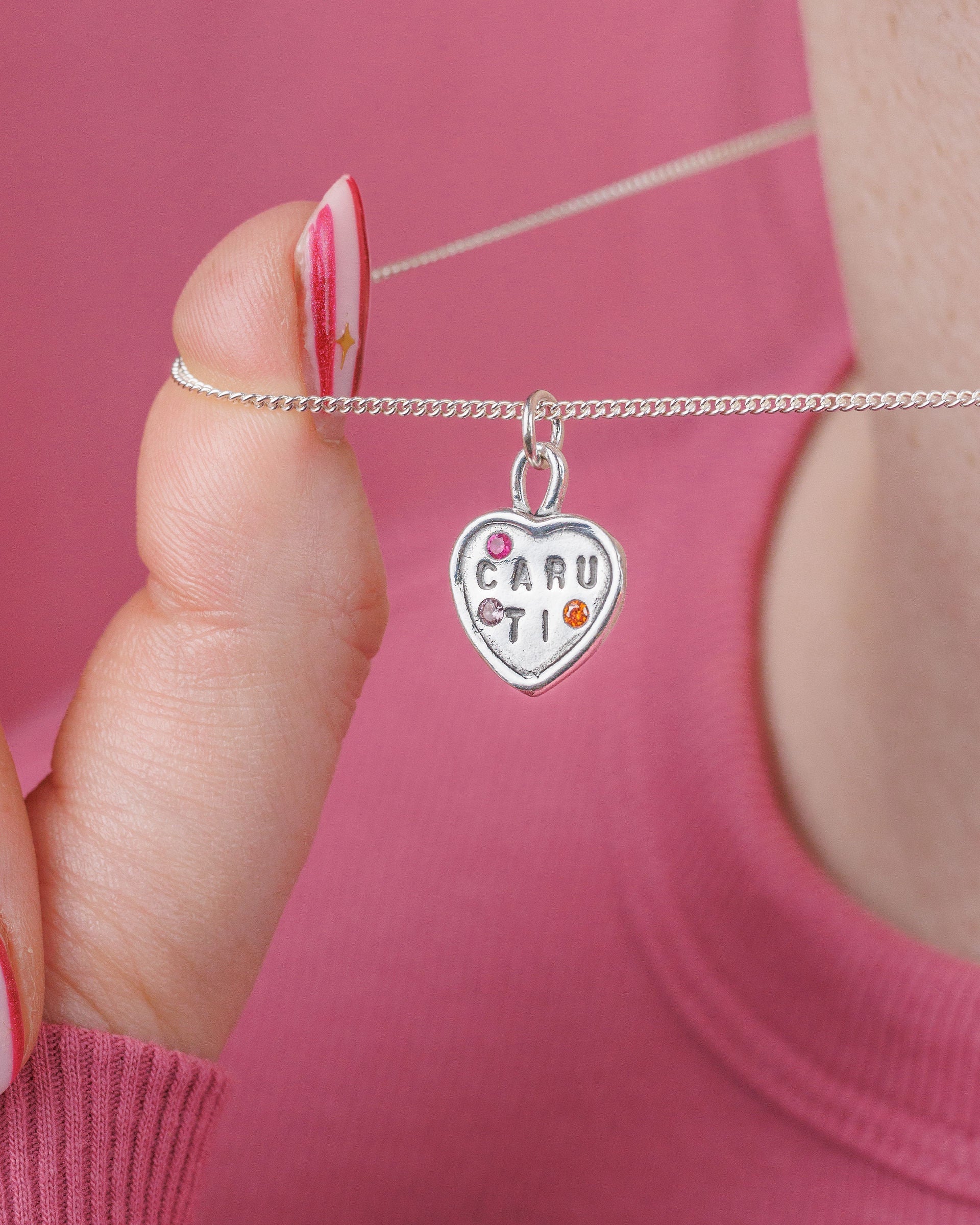 Necklace with a heart-shaped pendant held by a person wearing a pink top.