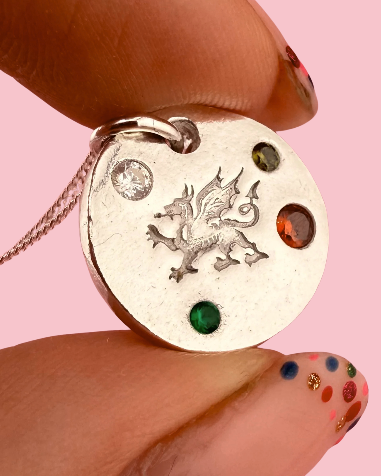 Silver pendant with Welsh dragon design held by a hand against a pink background