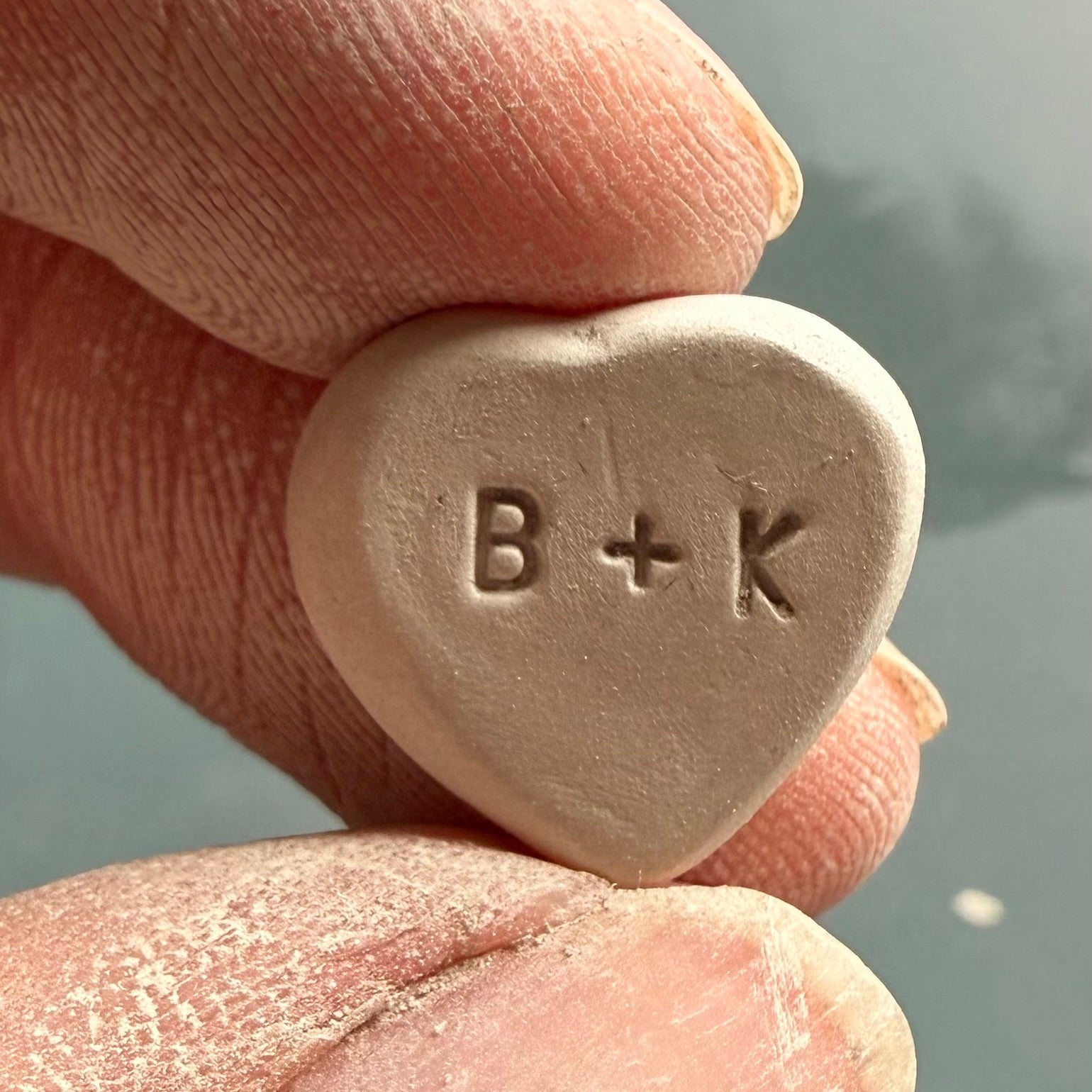 Heart-shaped object with 'B+K' engraving held between fingers against a blurred background