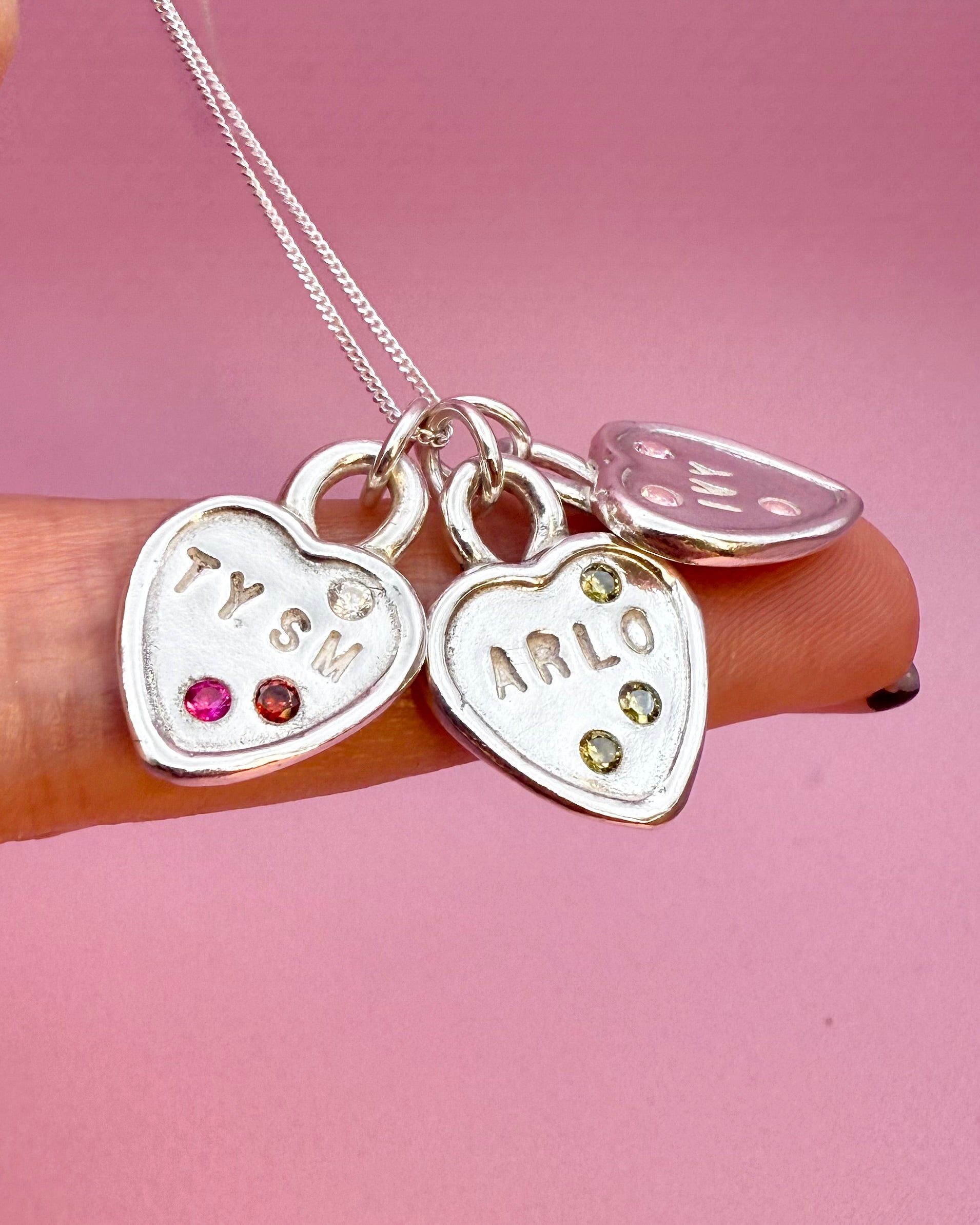 Silver heart-shaped charm necklace with engraved names on a pink background