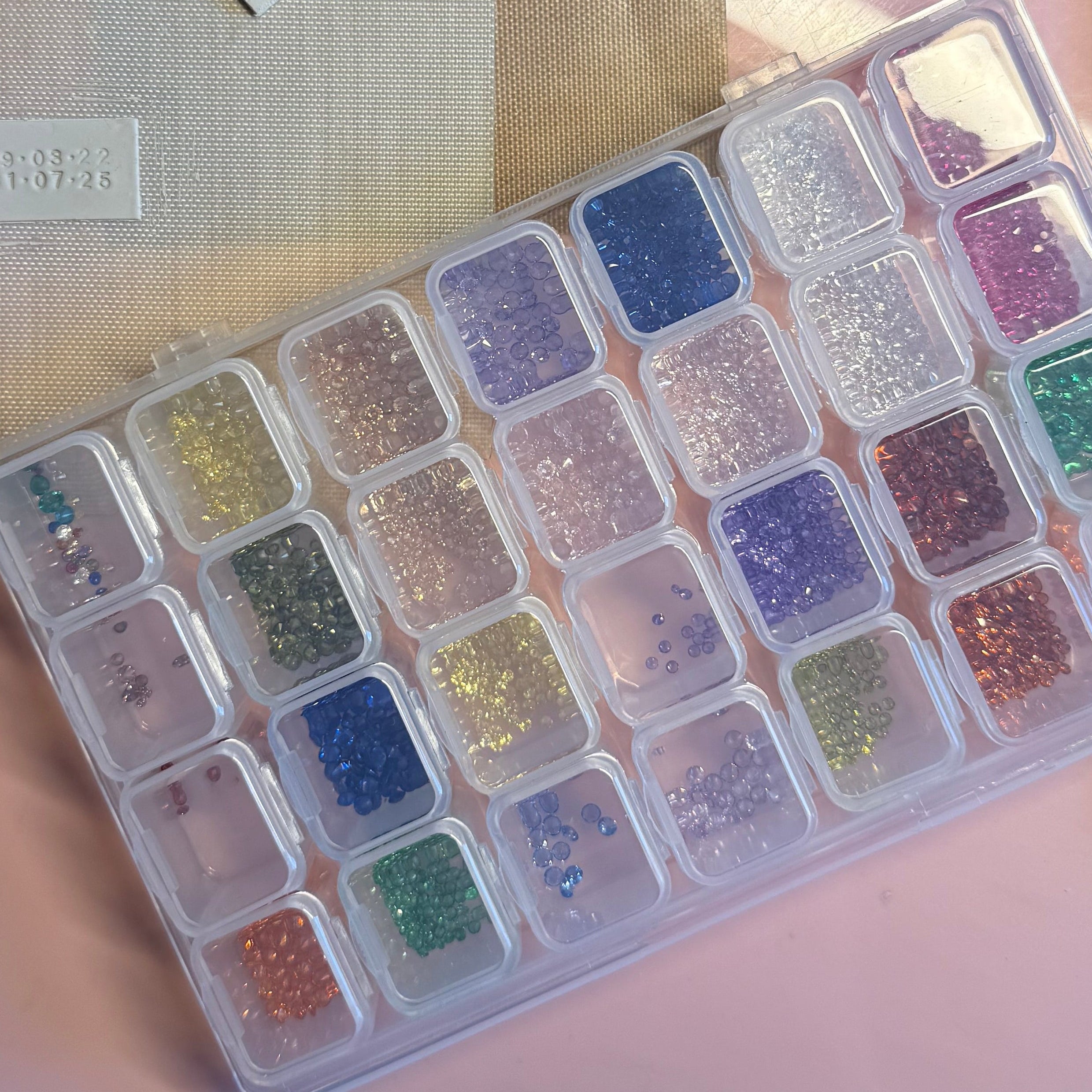 Container of cubic zirconia gemstones on a pink surface with tools and paper.