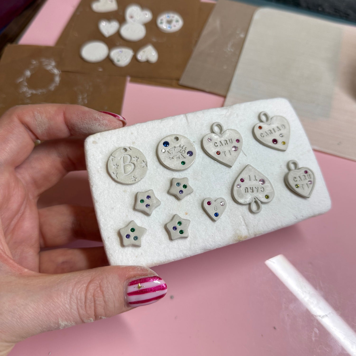Hand holding a a kiln shelf with dried silver clauy charms