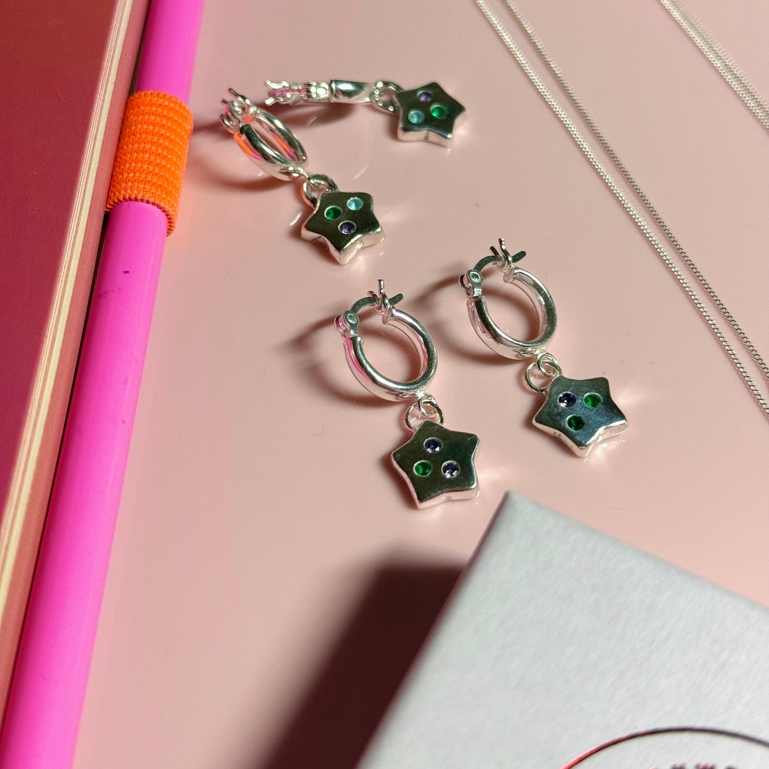 Star-shaped earrings with green stones on a pink surface
